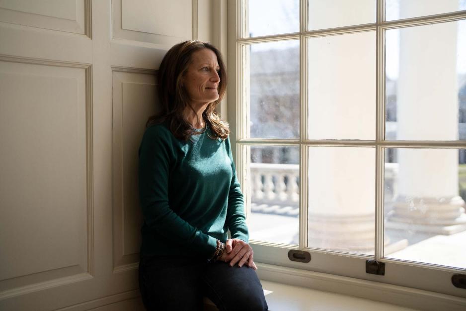 Maureen O'shea leaning agains a wall looking out a window.