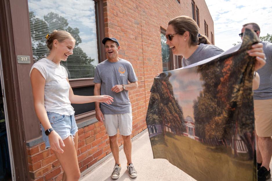 A student looks excitedly at a towel with a painting of the Rotunda and the Lawn held by her mother, as Jim Ryan laughs happily