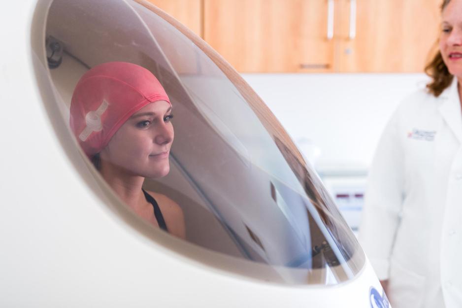 Student sitting inside a body mass pod while a doctor looks on