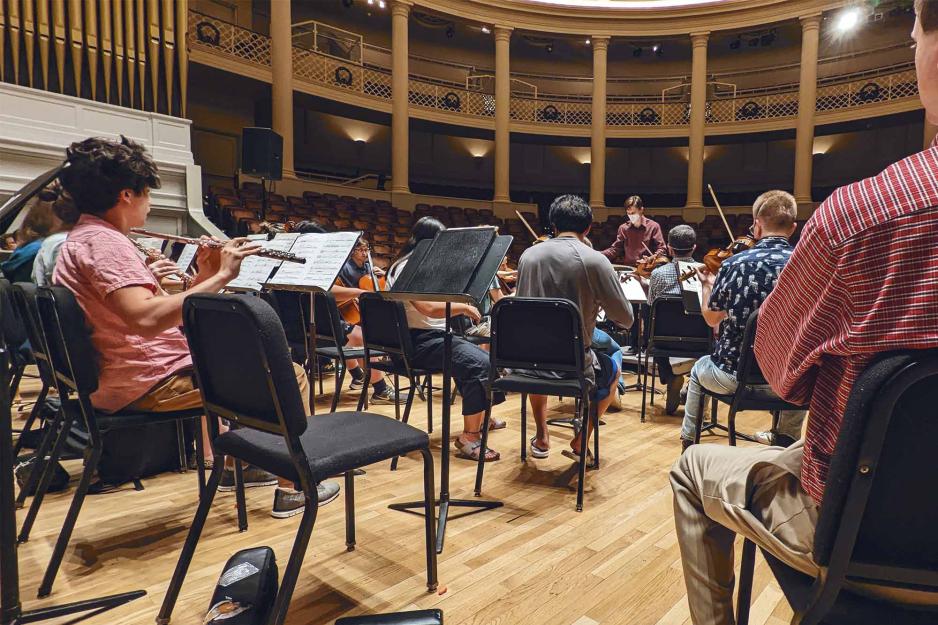 Seated musicians play stringed instruments in an auditorium