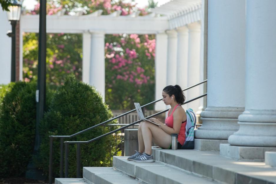 A student sitting outside on the steps of a building on a spring day