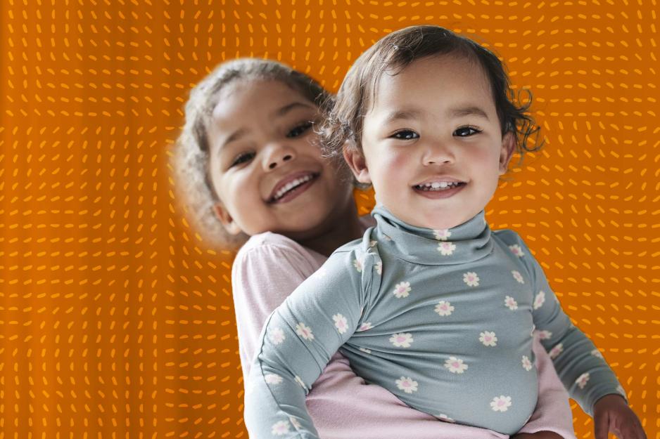 Two toddlers embrace over a textured orange background