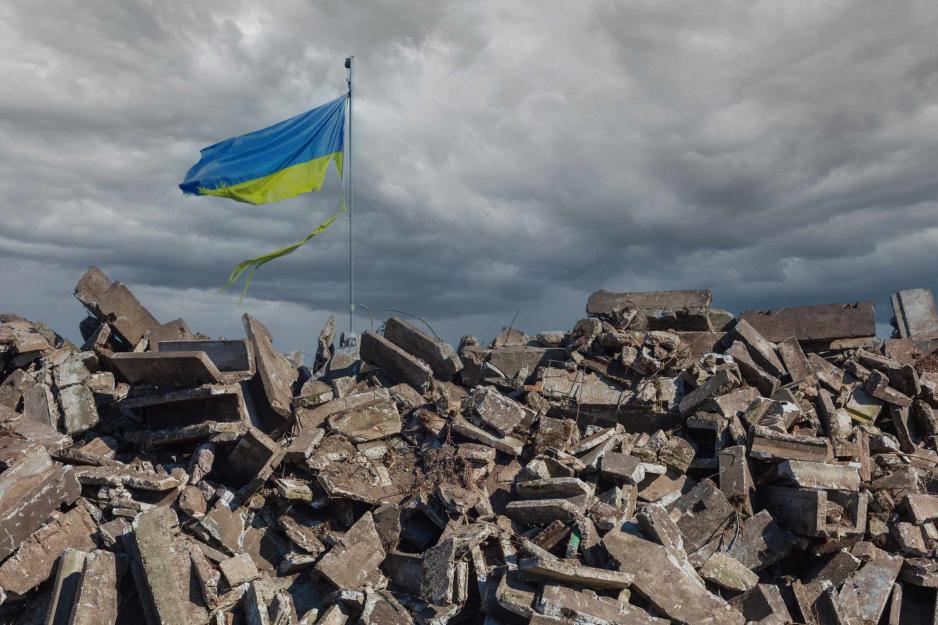 A Ukraine flag flying over piles of rubble as far as the eye can see
