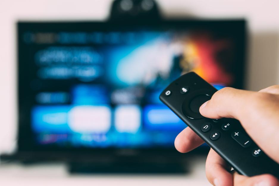 A hand holds a remote control in front of a television screen