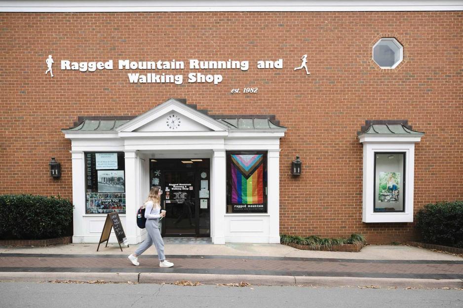 A woman walks past a storefront in a brick building with a sign reading 'Ragged Mountain Running and Walking Shop'