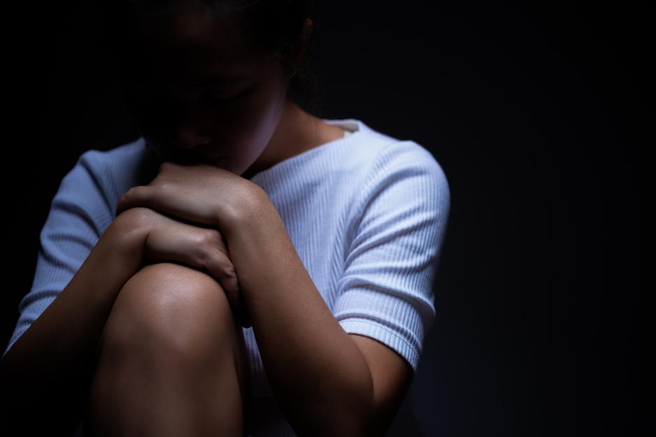 Woman in the shadows with hands on her knee and her head on her hands