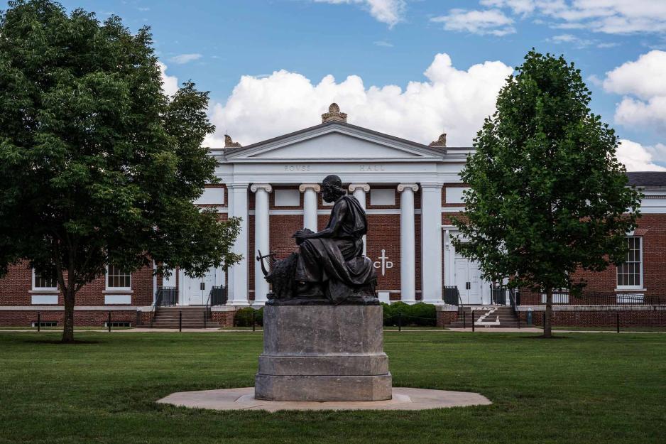 A statue of Homer In front of a building with pillars and the words "Rouss Hall" engraved on it. 