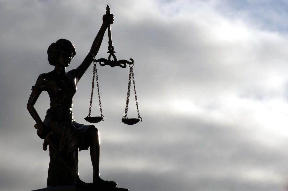 Silhouette of a statue of Lady Justice on a cloudy sky