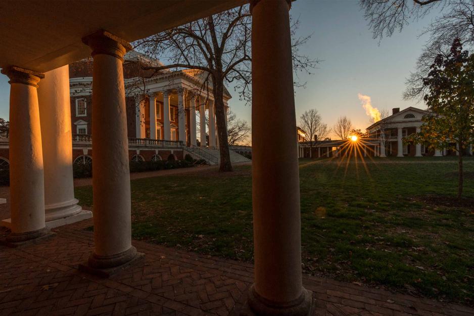 Looking from behind the columns of the west side of the lawn at the sun rising by the Rotunda