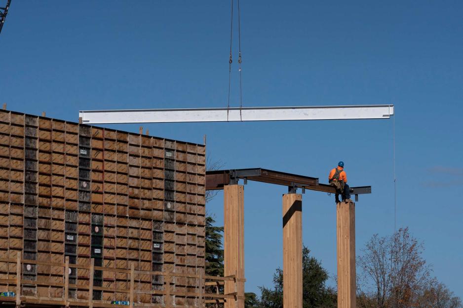 Crane lifting a huge white piece of metal topper on to three pillars