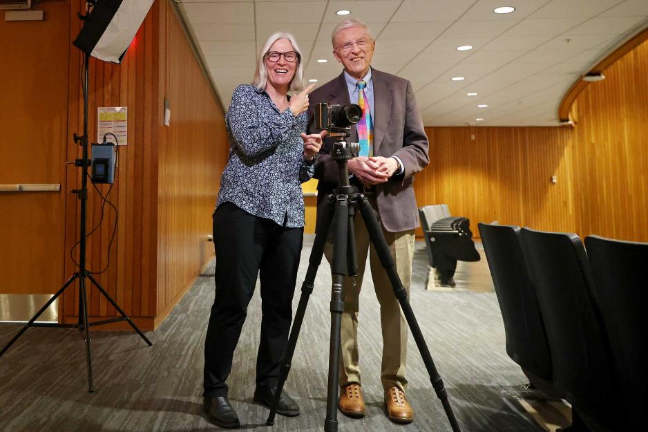 Ken Elzinga and Nancy Andrews stand together behind a camera on a tripod