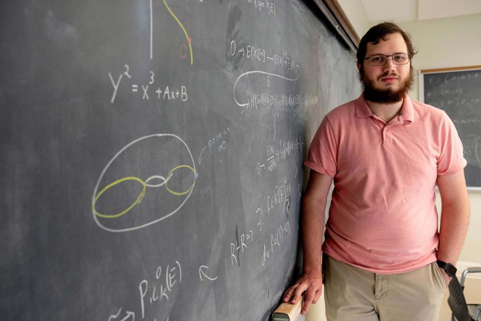 UVA student Spencer Martin stands in front of a chalk board covered in equations and graphs