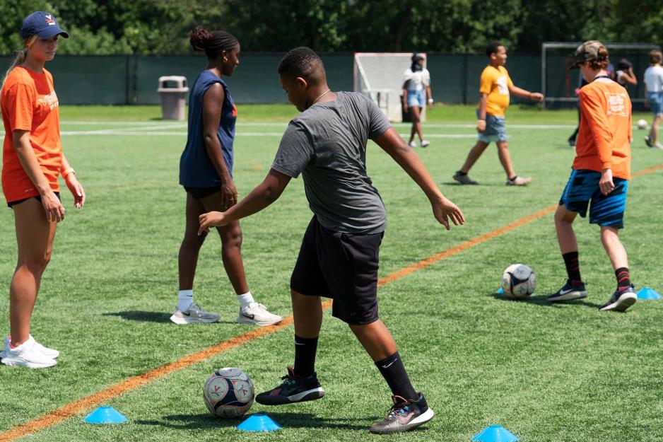 Several middle-school students practice dribbling soccer balls on a field