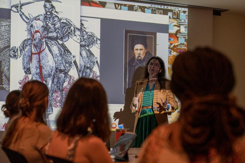 Tatiana Yavorska-Antrobius talks to a classroom of students next to a projection of a drawing of a man with a sword on horseback