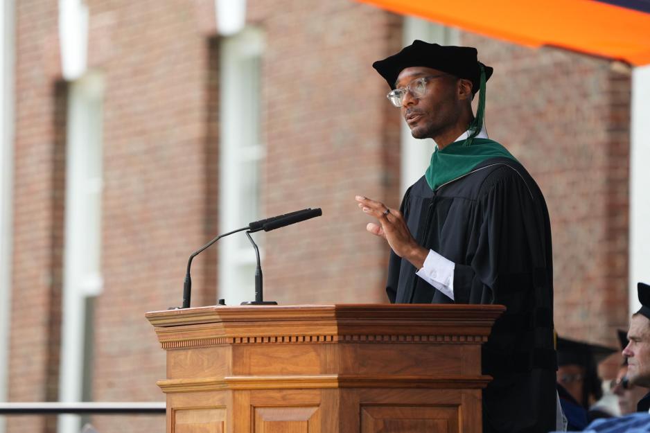 Dr. Taison Bell in ceremonial garb speaks from a wooden podium under a tent