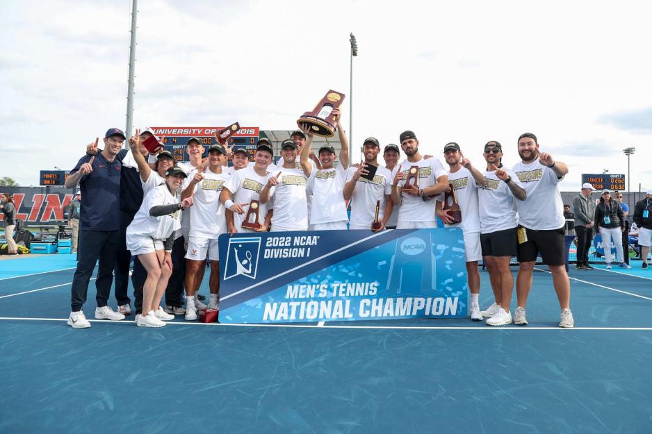 The UVA tennis team lines up for a group shot with the NCAA trophy and a sign reading '2022 NCAA Division 1 Men's Tennis National Champion'