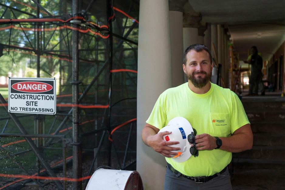 Travis Sly holds in hard hat in his hands as he stands in front the construction site on the Lawn.