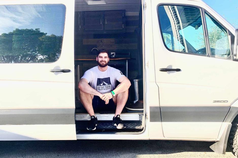 Nace Pleško sits in the doorway of his white van with his arms resting on his knees and smiling at the camera. 