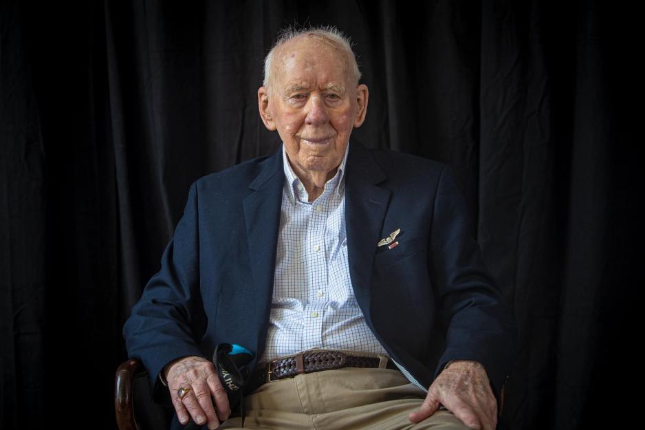 An elderly man in a blue blazer sitting in a chair, smiling
