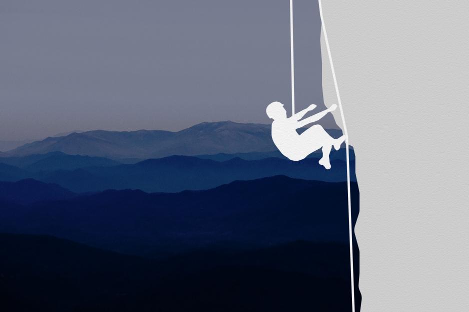 A person tethered to a rope scales the side of a cliff