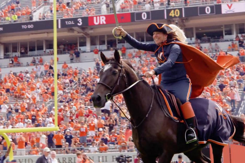 Julie riding a horse into Scott Stadium with Saber raised
