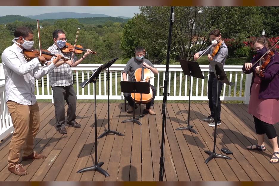 Group of string musicians play on a deck together 