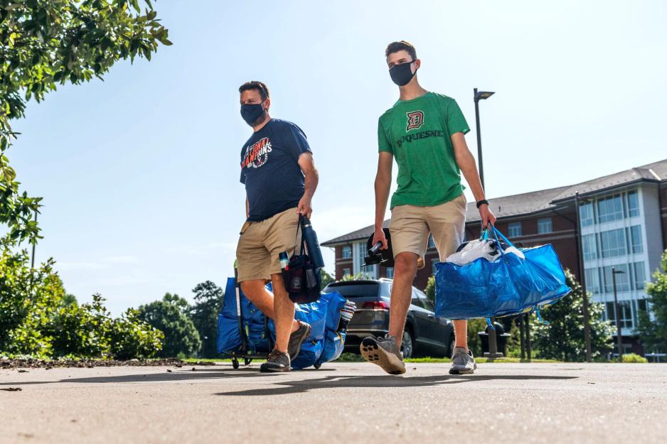 Father and son carrying bags of personal belongings into a dorm