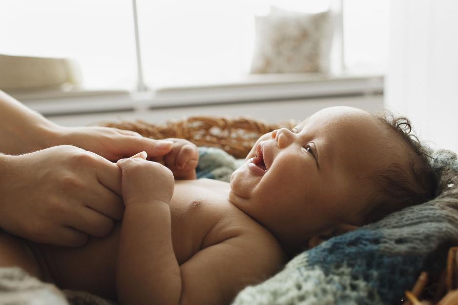 Baby laying in a blank while a woman hold its hands