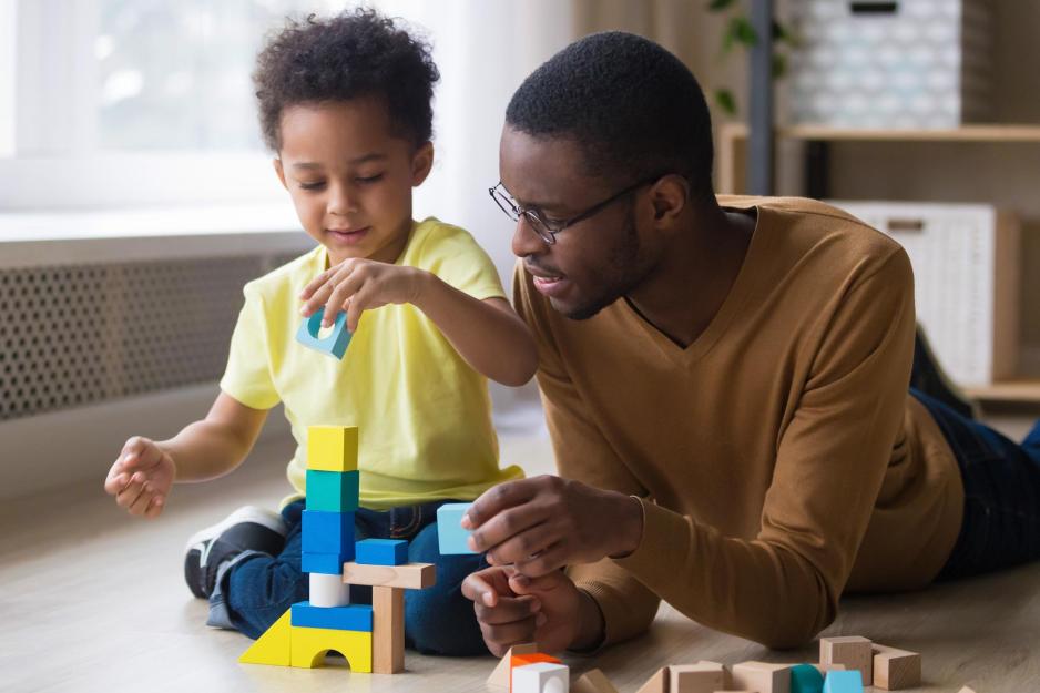 Man laying on the floor helping a child to build a tower with small multicolored building blocks
