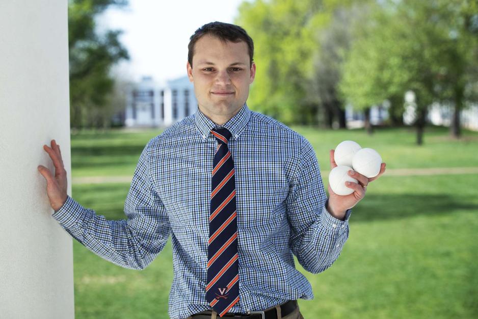 Chris Hodge standing holding three balls in his left hand and touching a white wall with his right hand