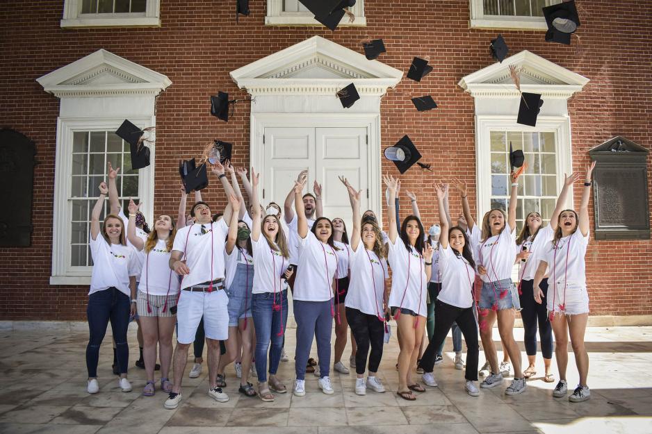 UVA students standing outside of a building on the Lawn and throw their caps into the air