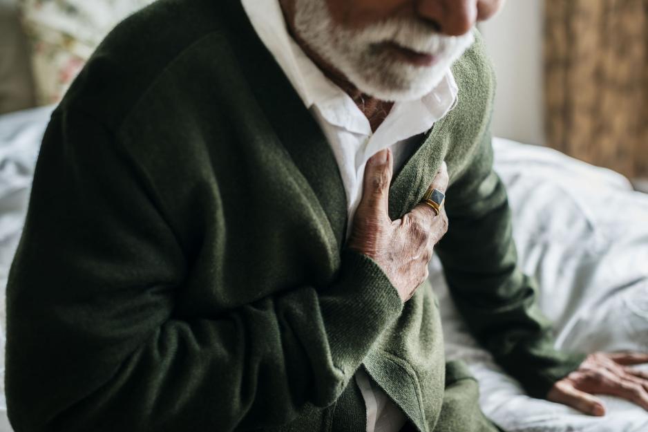 Older Adult grabbing their chest will sitting on the bed