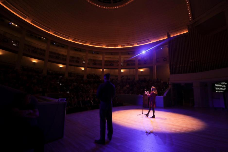  Sherri Moore standing on stage in the spotlight speaking to a crowd of people