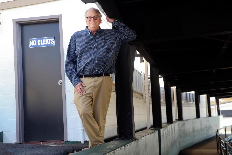 Doug Doughty standing in a stadium seating area near a door that reads No Cleats