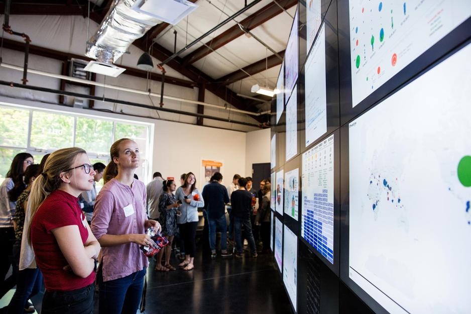 Students stand looking at monitors of various data being displayed