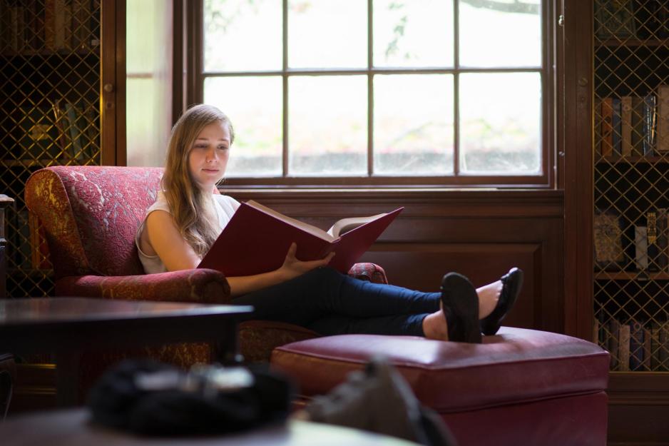 Student sitting in a chair with their feet propped up reading a book