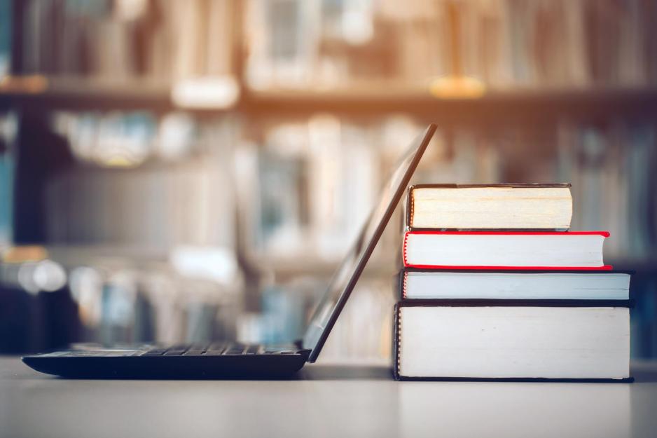 Laptop opened on a table with a stack of 4 books behind it
