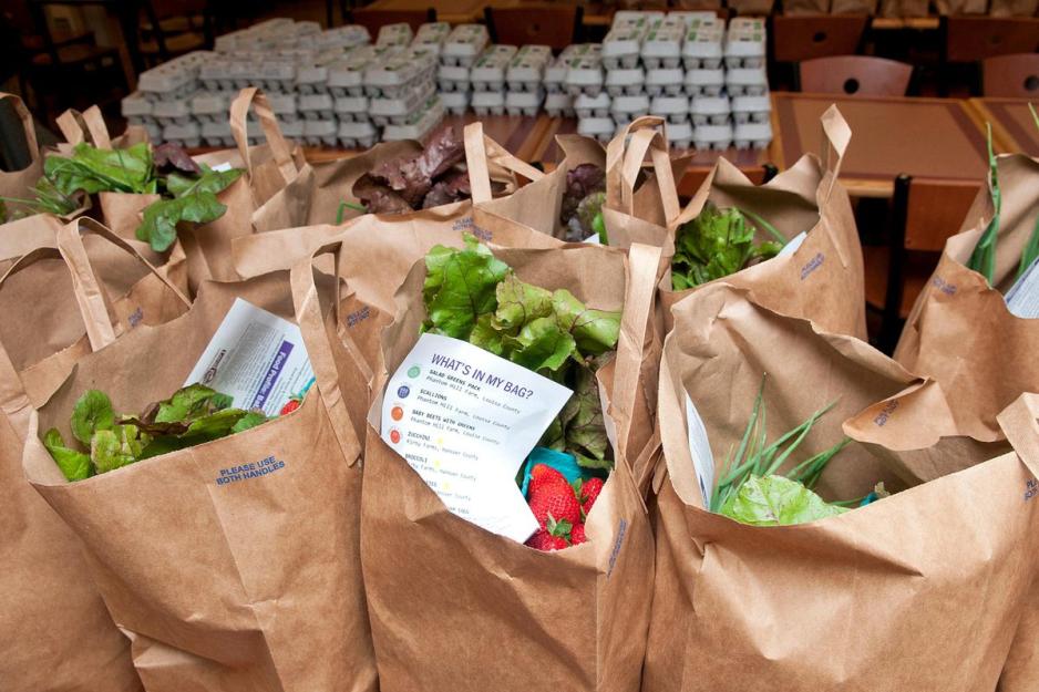 Brown paper bags filled with Vegetables and cartoons of eggs behind the bags on tables 