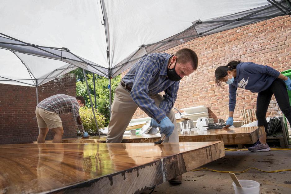 Tim Victorio, Mark Kutney and Youfang Duan smooth out epoxy on the poplar tabletops they are making