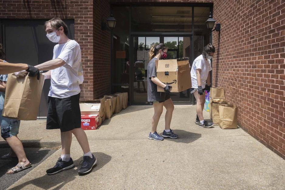 People handing out brown bags of supplies and other carrying boxes to set next to the brick wall on the sidewalk
