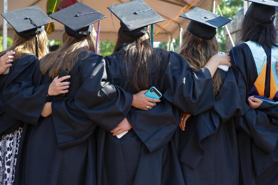 Group of UVA graduates on graduation day with arms wrapped around each others shoulders and backs posing for a picture
