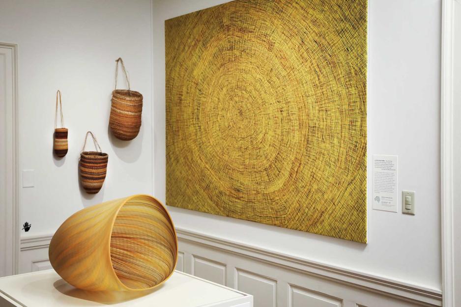 Aboriginal artwork, baskets handing on wall, cirrcled canvas painting on the wall, and a glass basket on an exhibit table