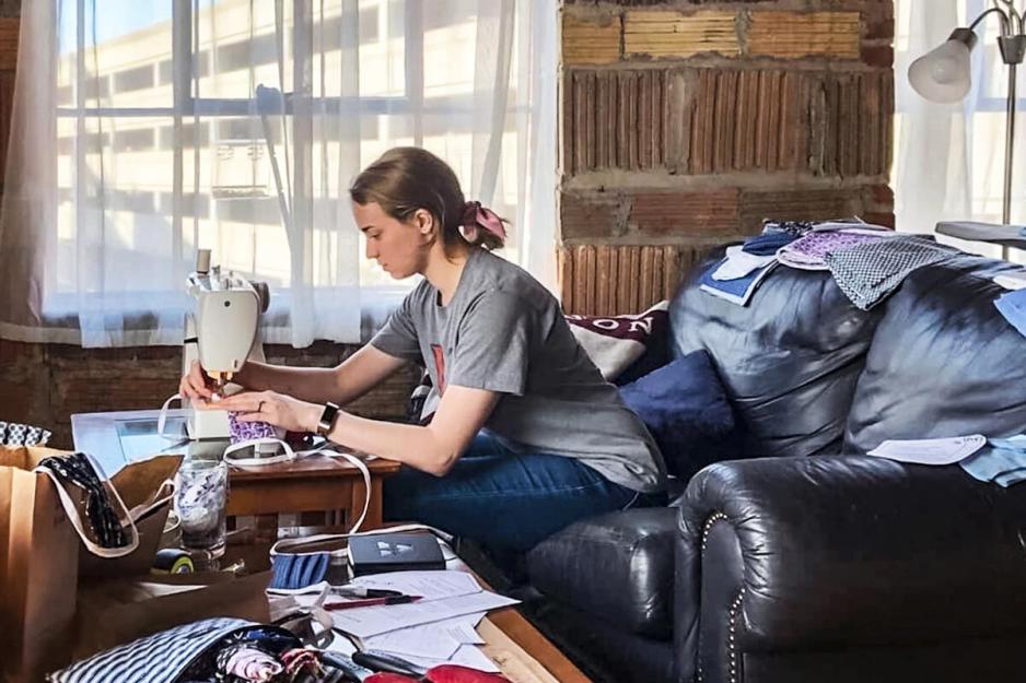 Julia Preziosi sits on her couch while sewing masks on a sewing machine