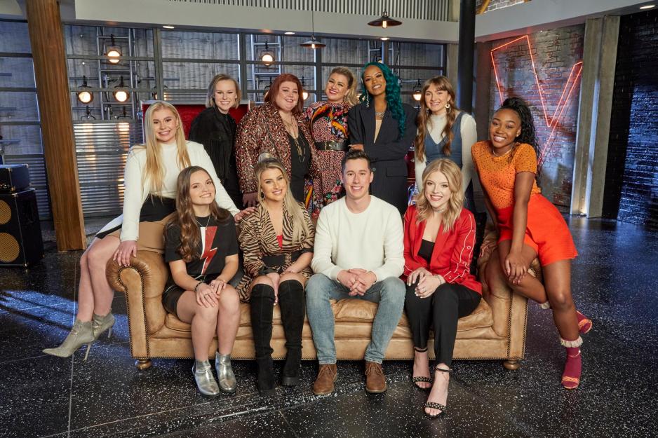 Micah Iverson (front, center) with Kelly Clarkson (back row, fourth from left) and the rest of the Kelly Clarkson team sitting on a couch and standing around the couch