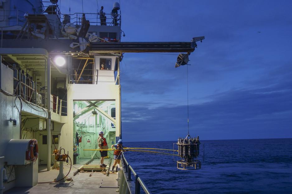 Crew on a boat using big yellow sticks to pull a big object that is hanging over the side