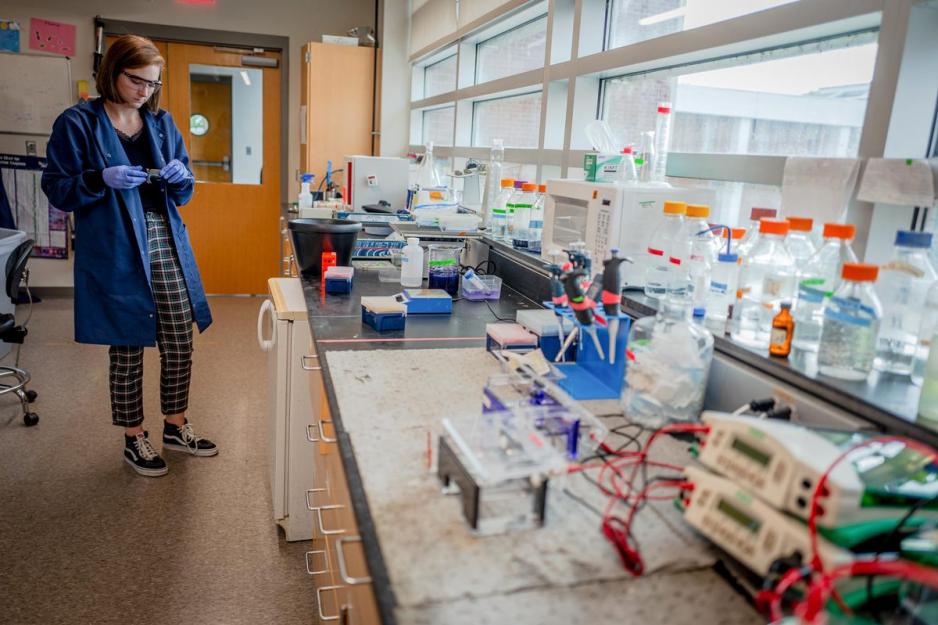 Madison Mann dressed in a lab coat holds a slide