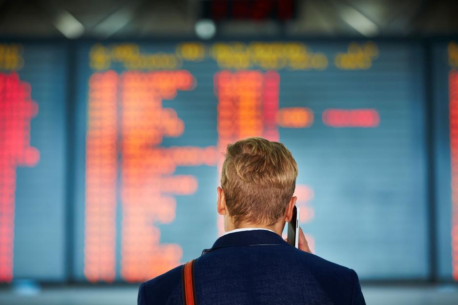 Man with cell phone to his ear looking at a travel board in an airport