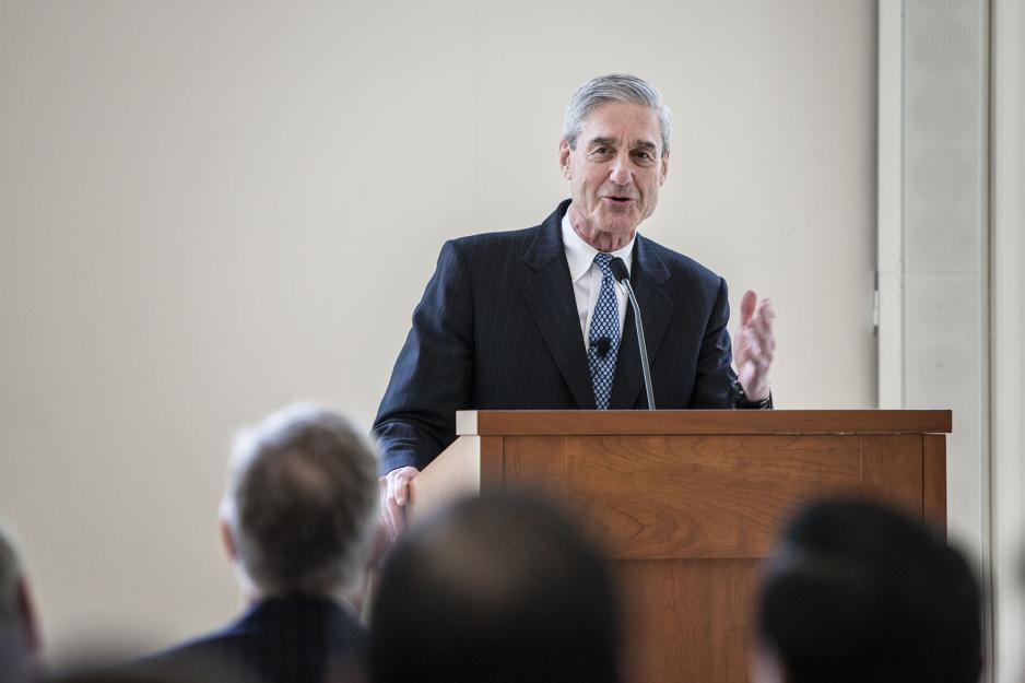 Robert Mueller speaking at a wooden podium to a crowd