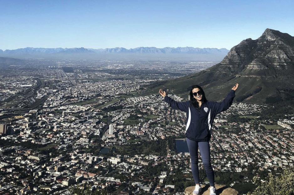 Sambriddi Pandey standing on the edge of a mountain with hands raised with a whole city below