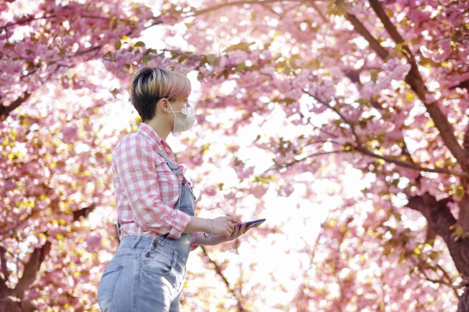 Woman wearing a mask outside as trees are blooming